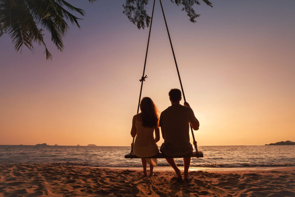 Paar auf einer Schaukel am Meer und Strand mit Sonnenuntergang